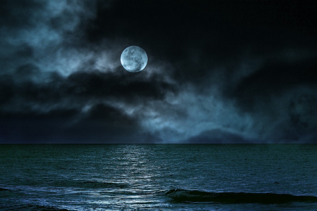 a full moon behind clouds above a still sea