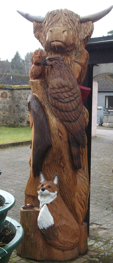 A wooden highland cow with bird of prey and fox
