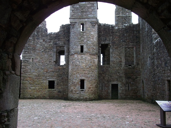the ruined walls of a castle and its courtyard seen through the arch of a large door