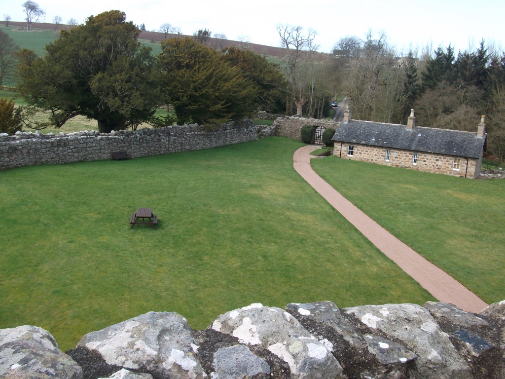 A view from the castle of the main path, a grass lawn and an old stone wall with trees beyond